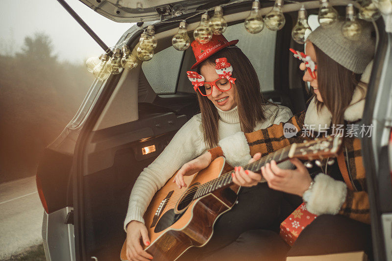 Two women in nature celebrate the new year - Two women in nature celebrate the new year - Two young women celebrate the new year by giving gifts, playing guitar and laugh out - Happy people .两个年轻女性在她们的车里庆祝新年，她们送礼物，弹吉他，放声大笑